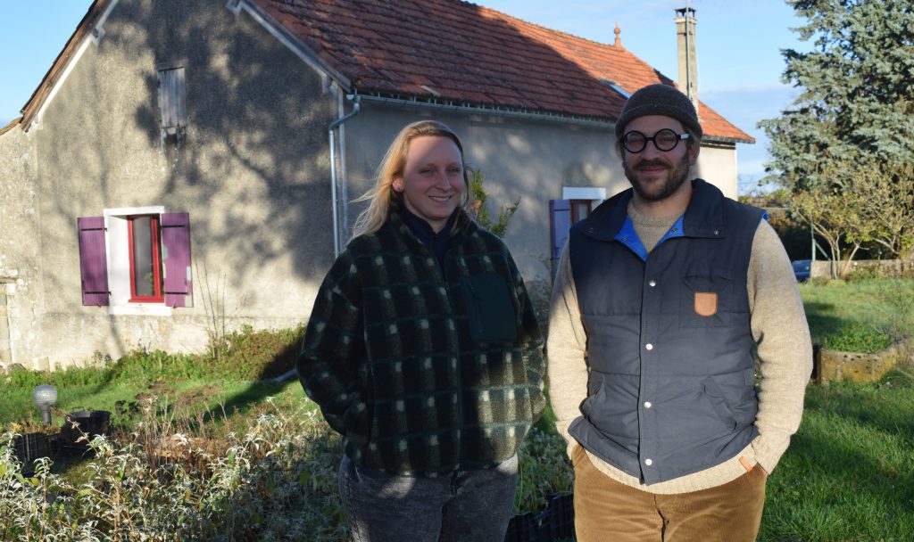 Marcelline Smetek, à gauche, et son mari Quentin Geffroy, à droite, posent devant la maison d'habitation, partie intégrante de l'exploitation qu'ils ont achetée en février 2021. À leurs pieds, quelques-uns des semis qu'ils ont effectués pour cette première année de travail.