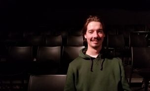 Un jeune homme souriant assis dans une salle de spectacle