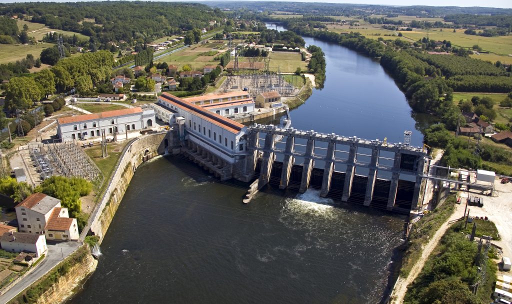Cette vue aérienne du barrage et de la centrale hydraulique de Tuilières, situés à Saint Capraise de Lalinde en amont de Bergerac (Dordogne), permet de voir l'étendue et la complexité des ouvrages sur la rivière, mais aussi la retenue d'eau créée en amont du barrage, les aménagements pour la population de poissons, la végétation abondante le long de la rivière dans les paysages périgordins.