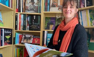 Une femme, Alix Breton, debout devant les rayonnages de e librairie tient un livre à la main