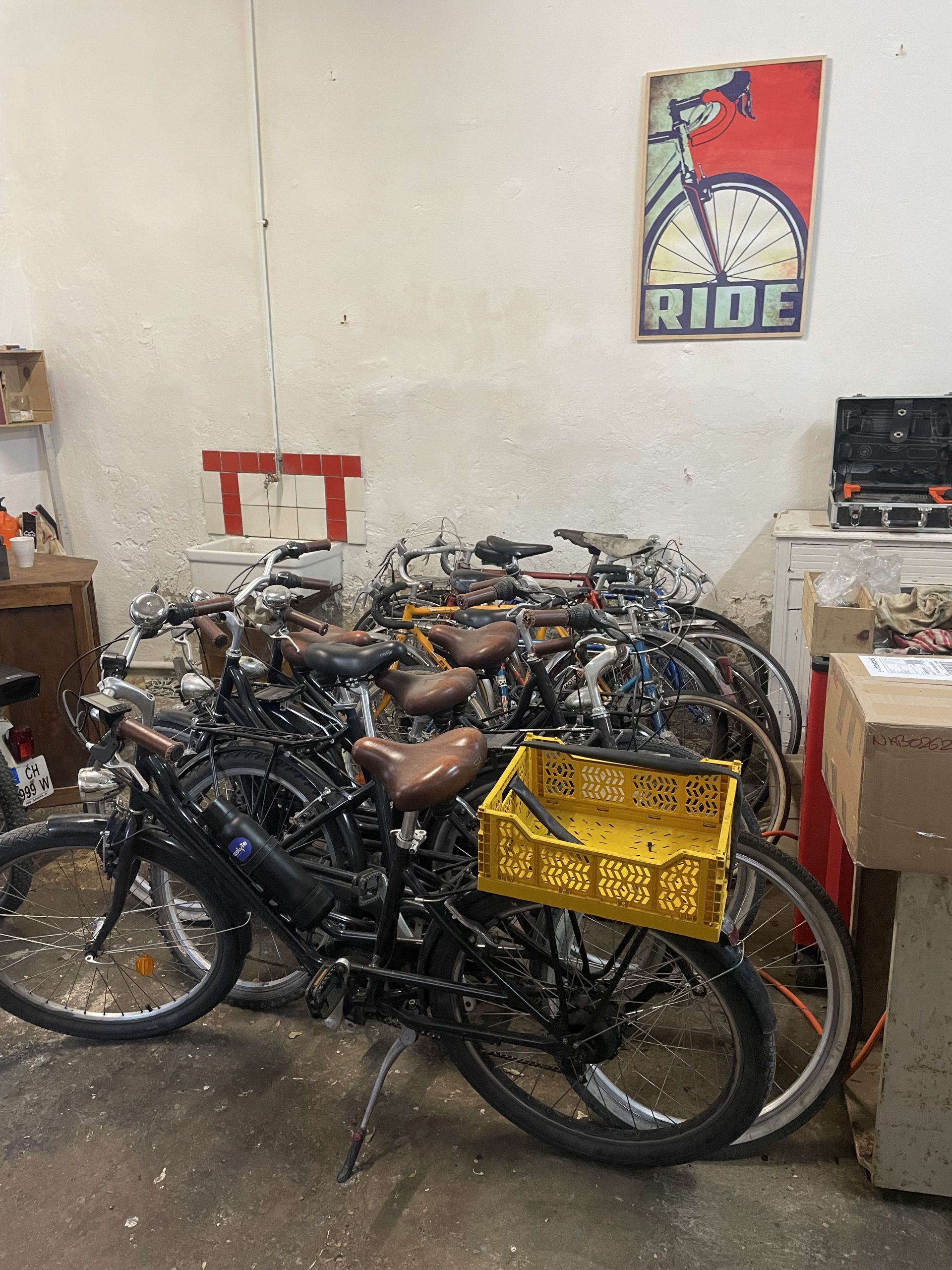 Le stock de vélos de Léonard, contre le mur de son garage, en attente de réparation ou d'électrification. Un cadre représentant une roue de vélo surplombe le tout.