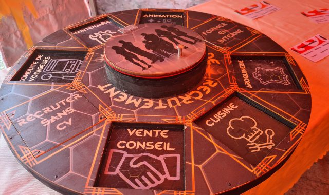 Une plaque ronde comportant des trous carrés, dans lesquels les participants de l'escape game doivent placer les plaques qu'ils auront trouvés grâce aux énigmes.