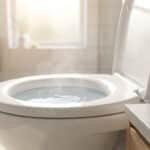 Toilettes blanches avec de l'eau qui fume dans la cuvette et une bouteille de vinaigre à côté, dans une salle de bain lumineuse.