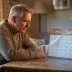 Un homme âgé et pensif regarde attentivement un calendrier de bureau ouvert sur octobre 2026, avec une date marquée.