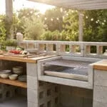 Cuisine extérieure DIY en parpaing et bois avec barbecue, légumes frais, herbes, vaisselle et guirlande lumineuse. Ambiance jardin.