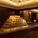 Pyramide de lingots d'or empilés sur un comptoir en marbre dans un cadre luxueux à Macao, avec des professionnels en arrière-plan.