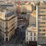 Vue aérienne de Paris montrant des immeubles haussmanniens, une barre d'immeuble moderne et un chantier de construction avec grue.