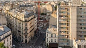 Vue aérienne de Paris montrant des immeubles haussmanniens, une barre d'immeuble moderne et un chantier de construction avec grue.