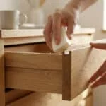 Gros plan sur des mains frottant un pain de savon blanc sur la glissière en bois d'un tiroir ouvert. Une astuce pour le débloquer.