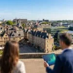 Vue de Rennes, mélange d'ancien et de moderne. Deux personnes, l'une tient une tablette avec un graphique de croissance symbolisant l'immobilier.