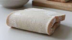 Gros plan sur deux tranches de pain de mie givrées sur une surface claire. Des cristaux de glace et de l'humidité sont visibles.