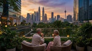 Couple de retraités profitant d'un verre sur une terrasse luxueuse à Kuala Lumpur, avec les tours Petronas et la tour KL au coucher du soleil.