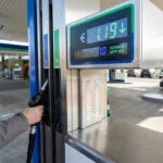 Une main saisissant un pistolet à essence dans une station-service affichant une réduction de prix en euros.