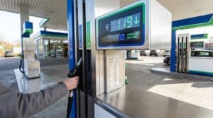 Une main saisissant un pistolet à essence dans une station-service affichant une réduction de prix en euros.