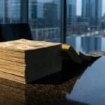Piles de billets de dollars américains sur une table sombre dans un bureau moderne avec vue sur la ville au crépuscule.