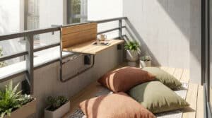 Une table pliante en bois fixée à la rambarde d'un balcon avec des coussins au sol et des plantes vertes.