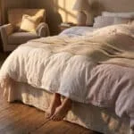 Pieds dépassant du bas d'un lit douillet dans une chambre baignée par la lumière dorée du soleil couchant.