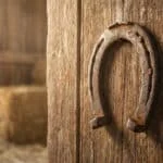 Un vieux fer à cheval rouillé est accroché, pointes vers le bas, sur une porte en bois vieilli dans une grange.