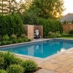 Une piscine moderne avec une pompe dissimulée derrière un écran en bois élégant dans un jardin arboré.