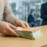 Mains déposant une épaisse liasse de billets en euros sur un comptoir bancaire dans une agence.