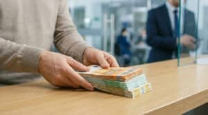Mains déposant une épaisse liasse de billets en euros sur un comptoir bancaire dans une agence.