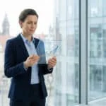 Une femme d'affaires examinant un écran holographique avec des graphiques de croissance devant une fenêtre de bureau.