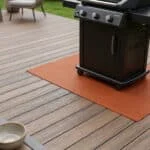 Barbecue noir posé sur un tapis de protection thermique orange sur une terrasse en composite.