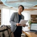 Un homme d'âge mûr regarde vers le haut dans un bureau, tenant des documents avec un sac de livraison à côté.
