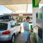 Un homme fait le plein de sa voiture chargée de bagages et de vélos dans une station-service.