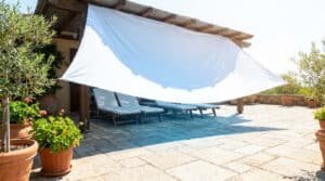 Un drap blanc tendu sous une pergola en bois pour créer de l'ombre sur une terrasse en pierre avec des transats.