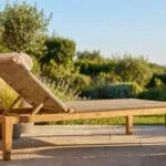 Transat de jardin en bois de teck et assise en corde tressée sur une terrasse ensoleillée entourée de plantes.