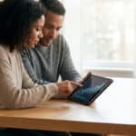 Un couple consulte un graphique financier sur une tablette numérique autour d'une table en bois.