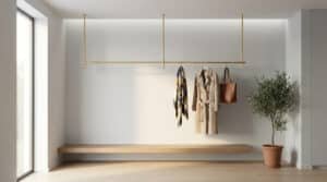 Tringle de penderie minimaliste en laiton doré fixée au plafond au-dessus d'un banc en bois dans une entrée épurée.