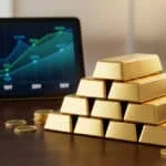 Lingots d'or empilés en pyramide sur une table devant une tablette affichant une courbe de croissance financière.