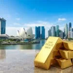 Lingots d'or empilés sur une surface en marbre avec en arrière-plan la skyline moderne de Singapour sous un ciel bleu.