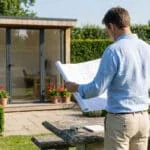 Un homme examine des plans devant un studio de jardin moderne dans un jardin paysager.
