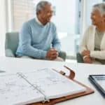 Un couple de retraités souriant discutant à côté d'un agenda 2026 ouvert et d'une tablette.