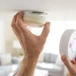 Une personne retire un vieux détecteur de fumée du plafond pour en installer un nouveau.