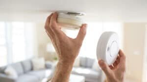Une personne retire un vieux détecteur de fumée du plafond pour en installer un nouveau.