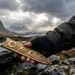 Une main gantée tient un ornement en or finement ciselé avec des motifs anciens dans un paysage montagneux norvégien.