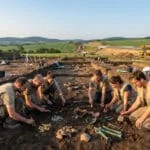 Équipe d'archéologues travaillant sur un site de fouilles en République tchèque avec des objets anciens au premier plan.
