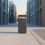 Une poubelle urbaine grise isolée sur un trottoir au milieu d'immeubles modernes.