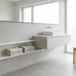 Salle de bain moderne avec meuble vasque suspendu, étagère encastrée et tabouret en bois clair.